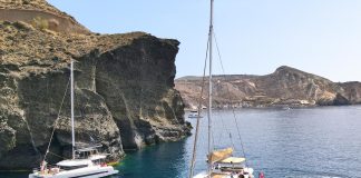 What to Expect and How to Book a Santorini Cruise Catamaran sailing past the Indian rock in Santorini Greece