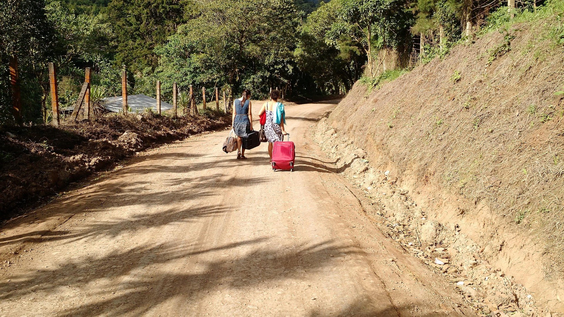 Travelers with luggage on a dirt road.