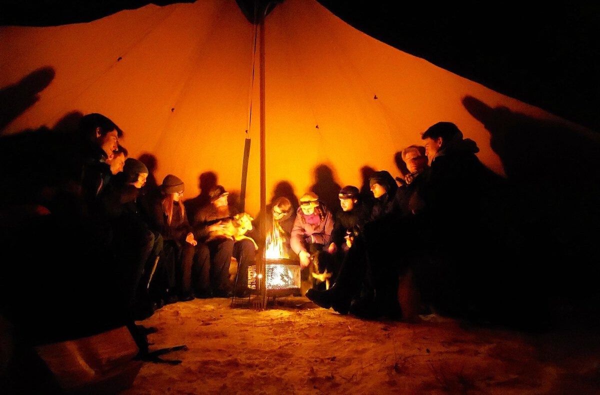 hiking with huskies in abisko - An Evening Walk With Huskies Guests gathered around a warm fire inside a traditional lávvu during a guided husky hike in Abisko, Swedish Lapland.